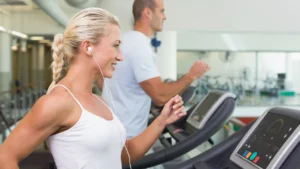 Donna di circa 50 anni corre sul tapis roulant in palestra con le cuffie, esempio di allenamento in Zona 2
