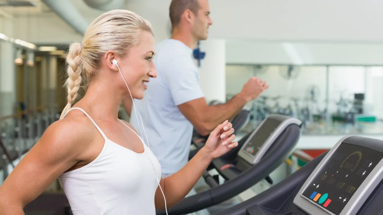 Donna di circa 50 anni corre sul tapis roulant in palestra con le cuffie, esempio di allenamento in Zona 2